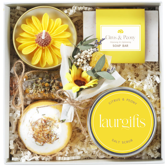 A gift box containing yellow and white bath products. It features a sunflower candle, soap, salt scrub, and a bath bomb. The box is filled with shredded paper and tied with a yellow ribbon, creating a spa-like theme.